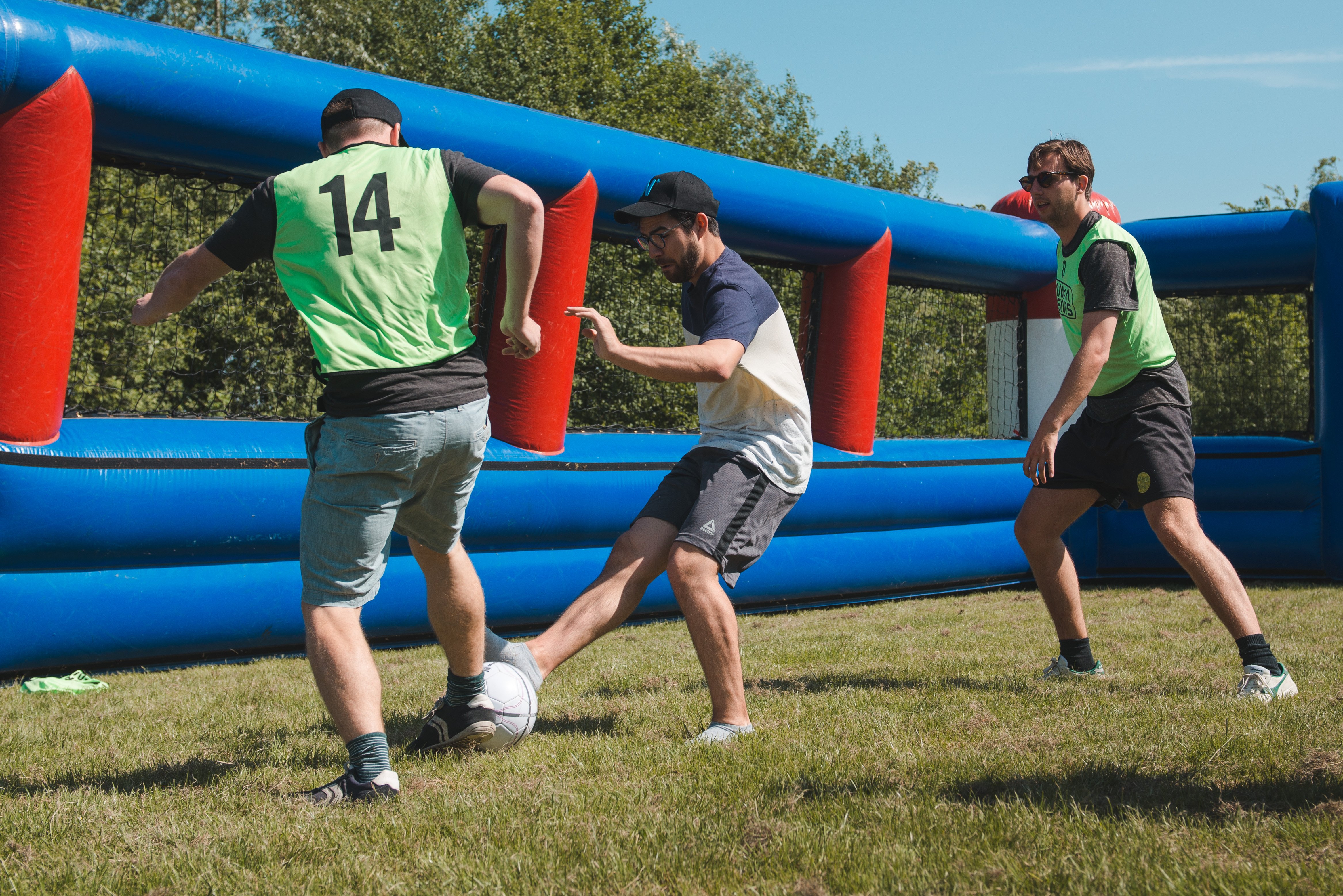 Tiago plays football with two other colleagues on a grass field.